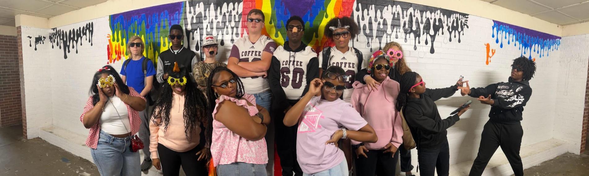 A group of students pose in front of a painted brick wall