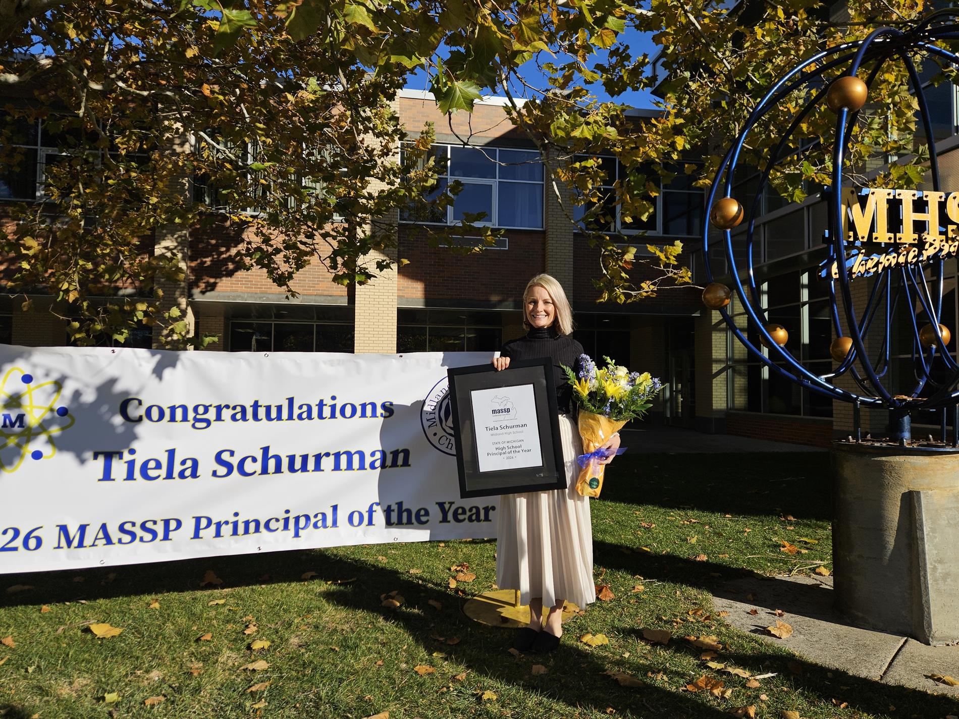 Tiela Schurman holds her award while standing in front of a banner at Midland High School