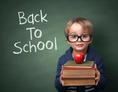 young boy standing in front of a chalkboard that says Back to School. He is holding books with an apple on top.