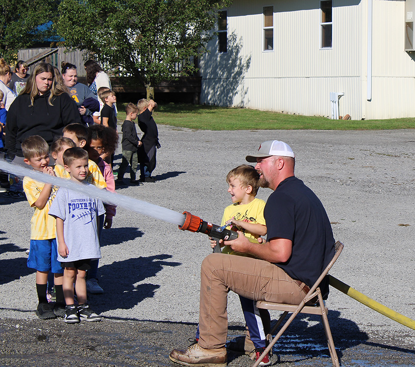 Fire Fighter Andrew Russell helps students with the fire hose