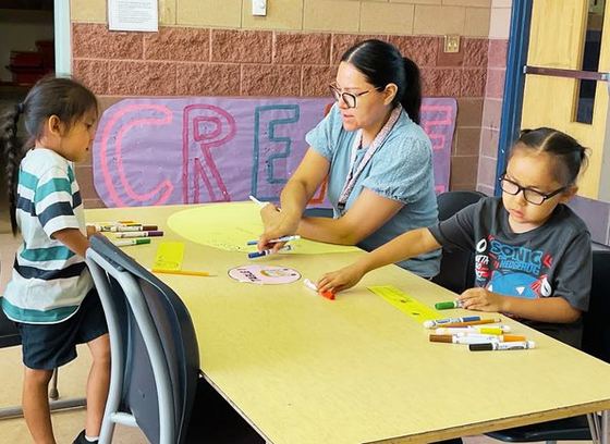 An art teacher working with a student at a table of markers and paper
