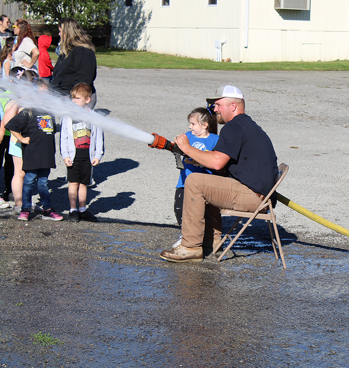 Fire Fighter Andrew Russell helps students with the fire hose