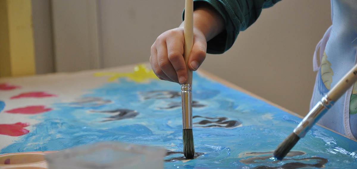 A small child paints with a pinatbrush on a paper A small child paints with a pinatbrush on a paper