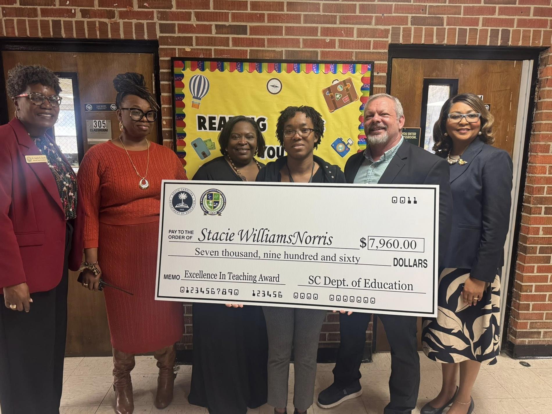 people standing in hallway holding large check 