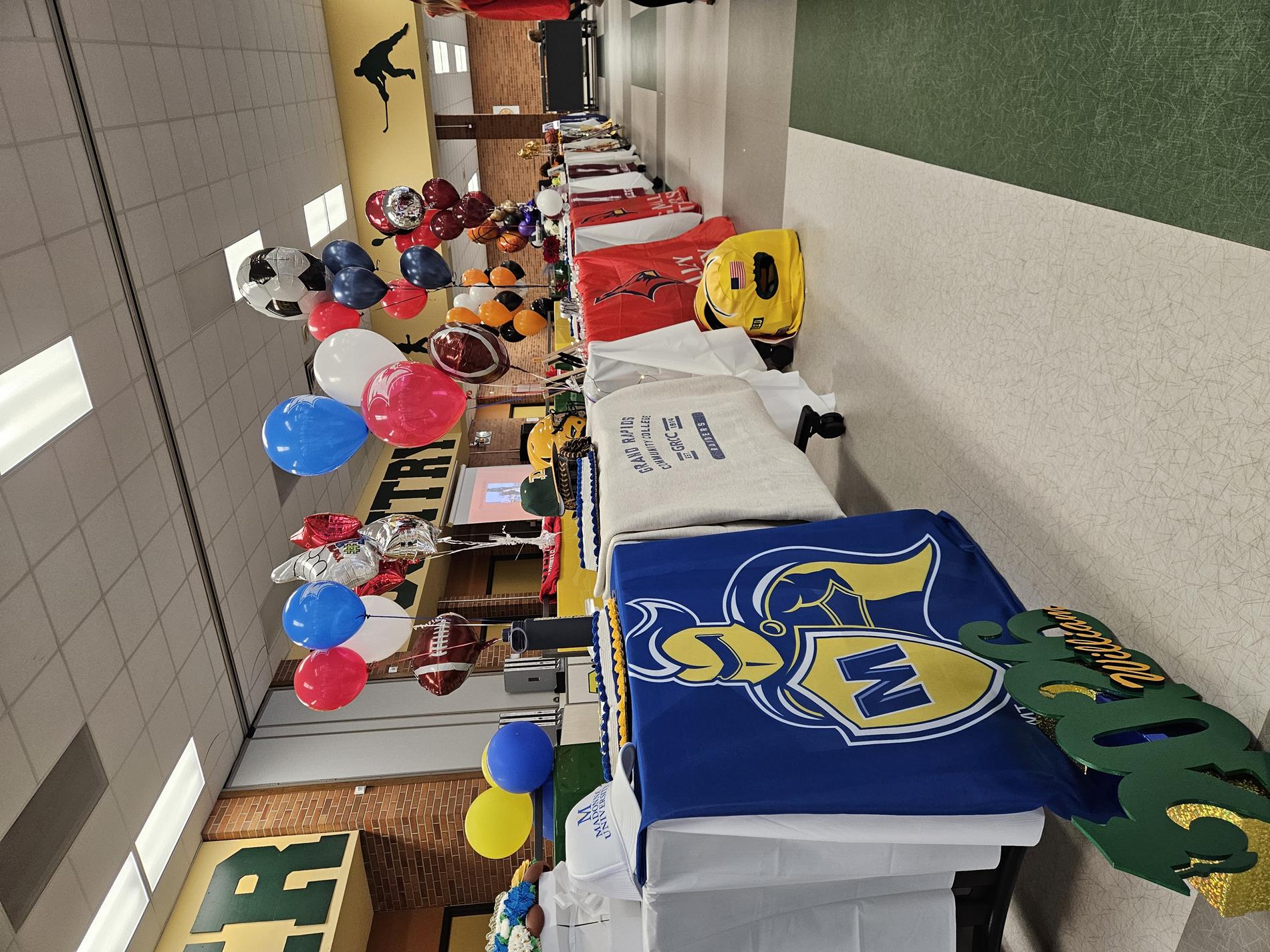 A group of tables in the Dow High School cafeteria with balloons and banners for each of the athletes' universities