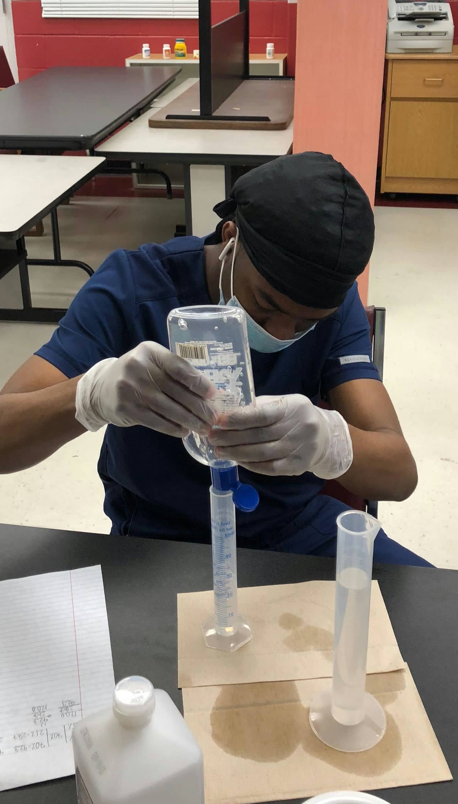 A pharmacy technician student pouring liquid into a cylinder