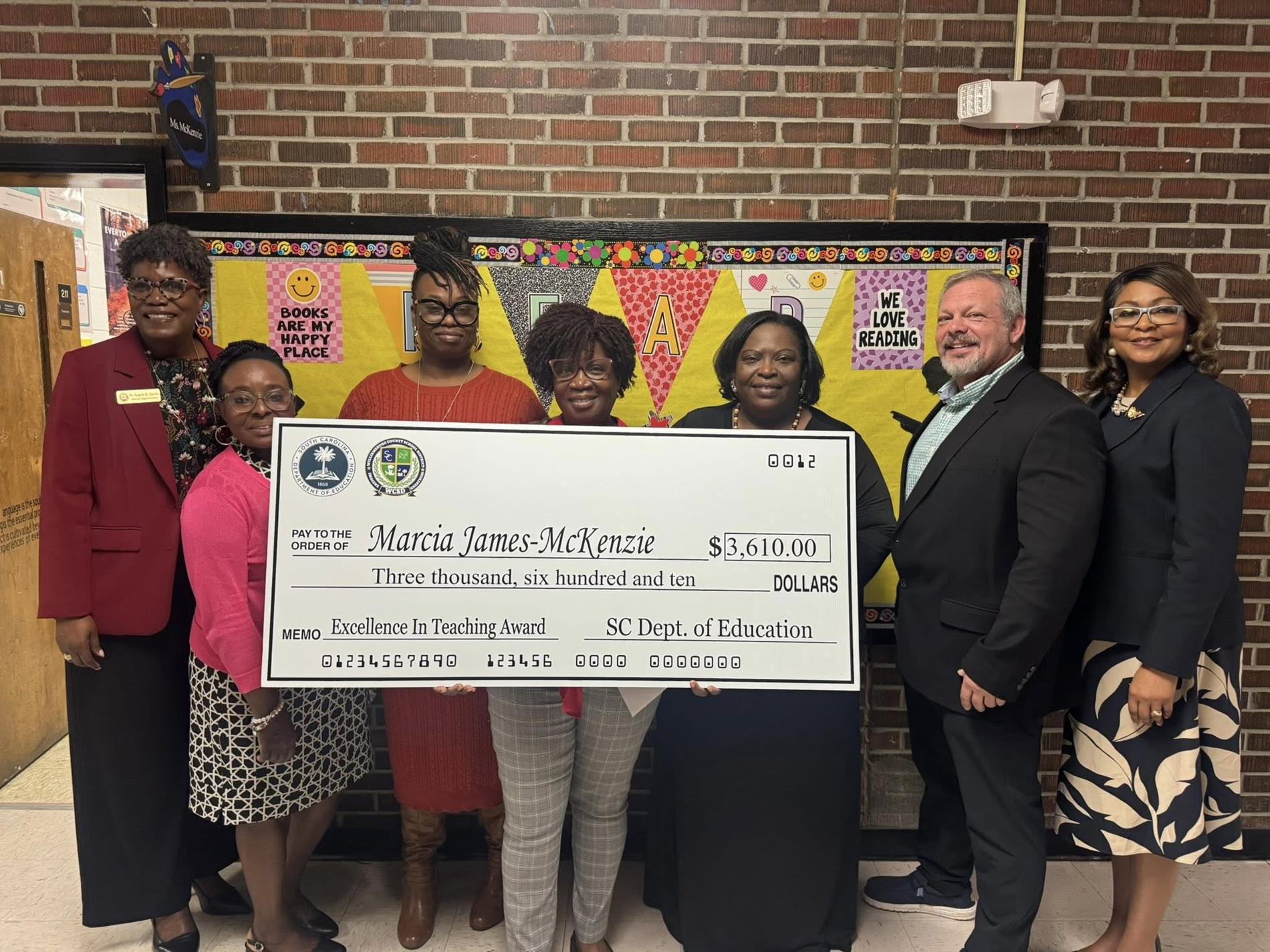 people standing in hallway holding large check 