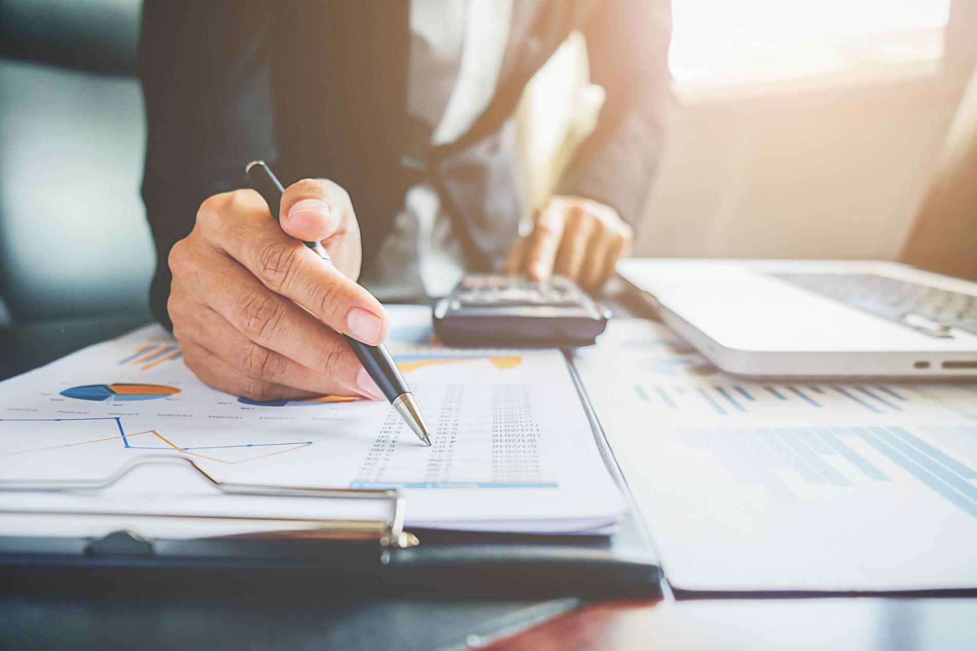 A man leans over a budget document with a pen and a calculator