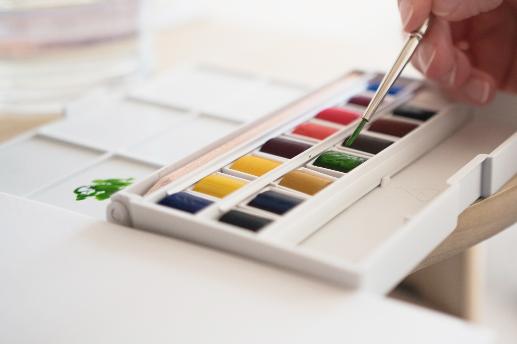 A person's hand holding a brush dipped in watercolor paint.