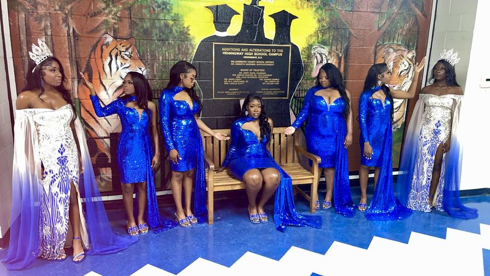 female homecoming contestants standing and sitting in front of tiger mural 