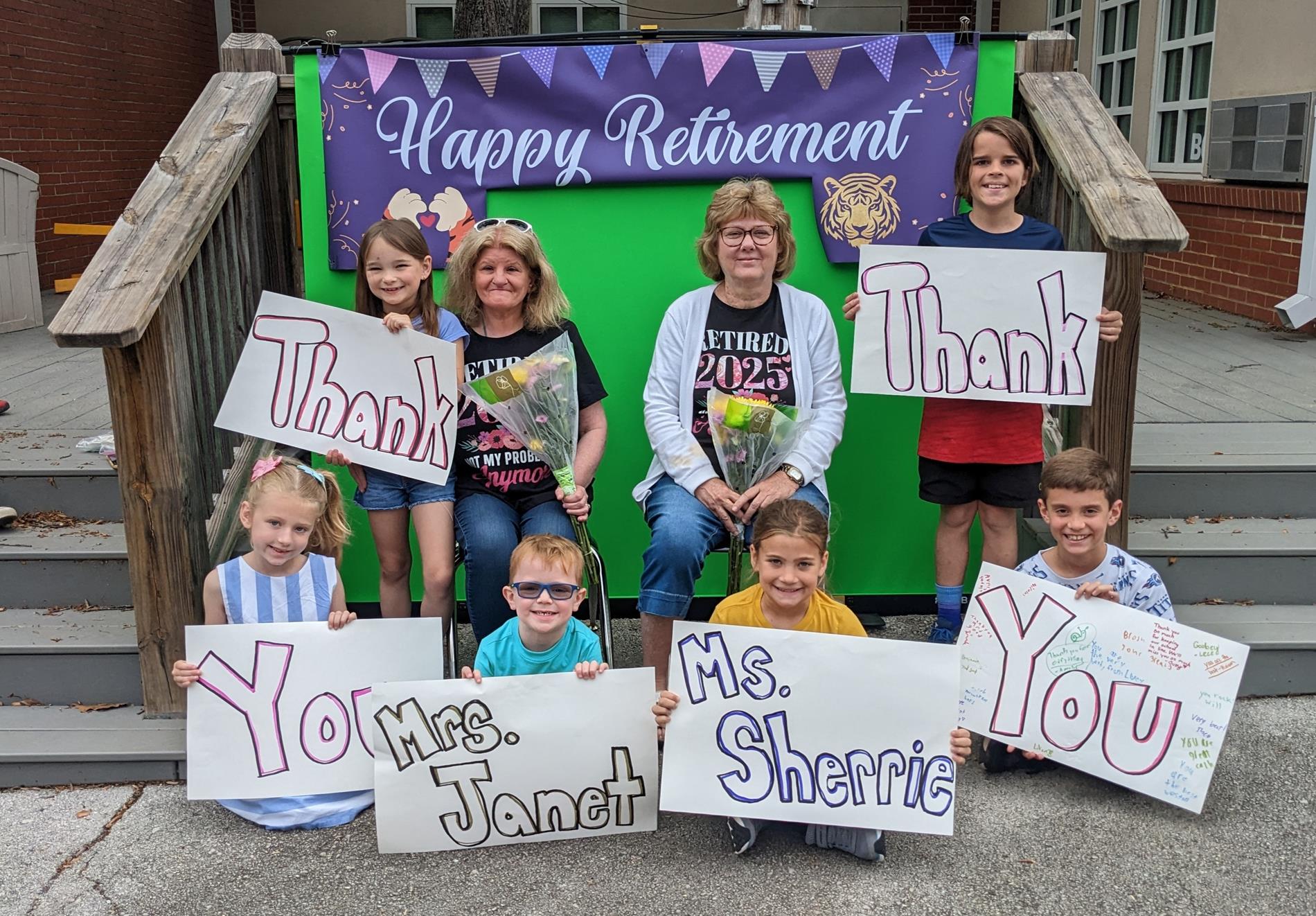 students holding thank you cards and a happy retirement banner for two staff members at elementary school