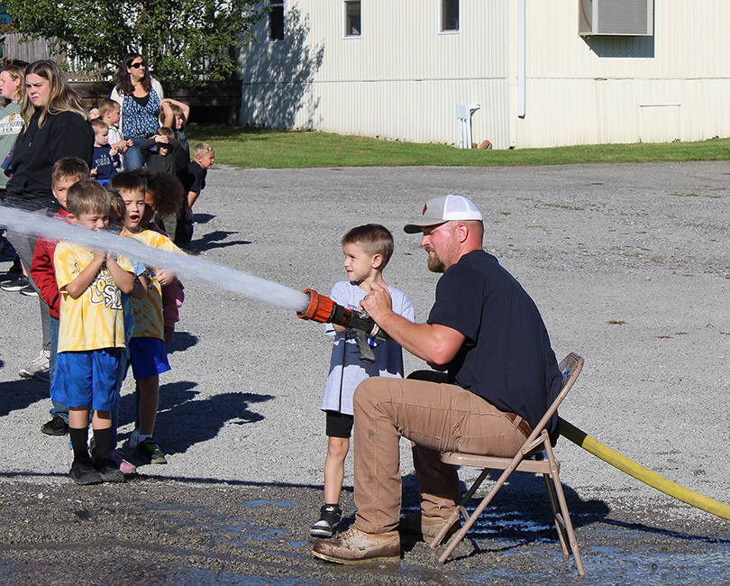 Fire Fighter Andrew Russell helps students with the fire hose