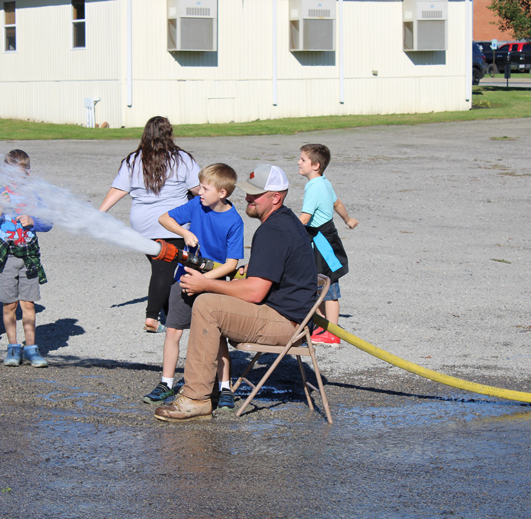 Fire Fighter Andrew Russell helps students with the fire hose