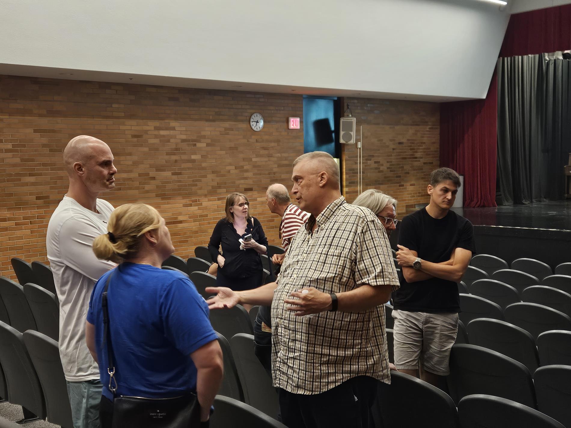 Two men and a women stand in the auditorium chatting about the presentation