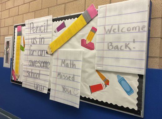 A classroom bulletin board reading Welcome Back with pencil and crayon cutouts