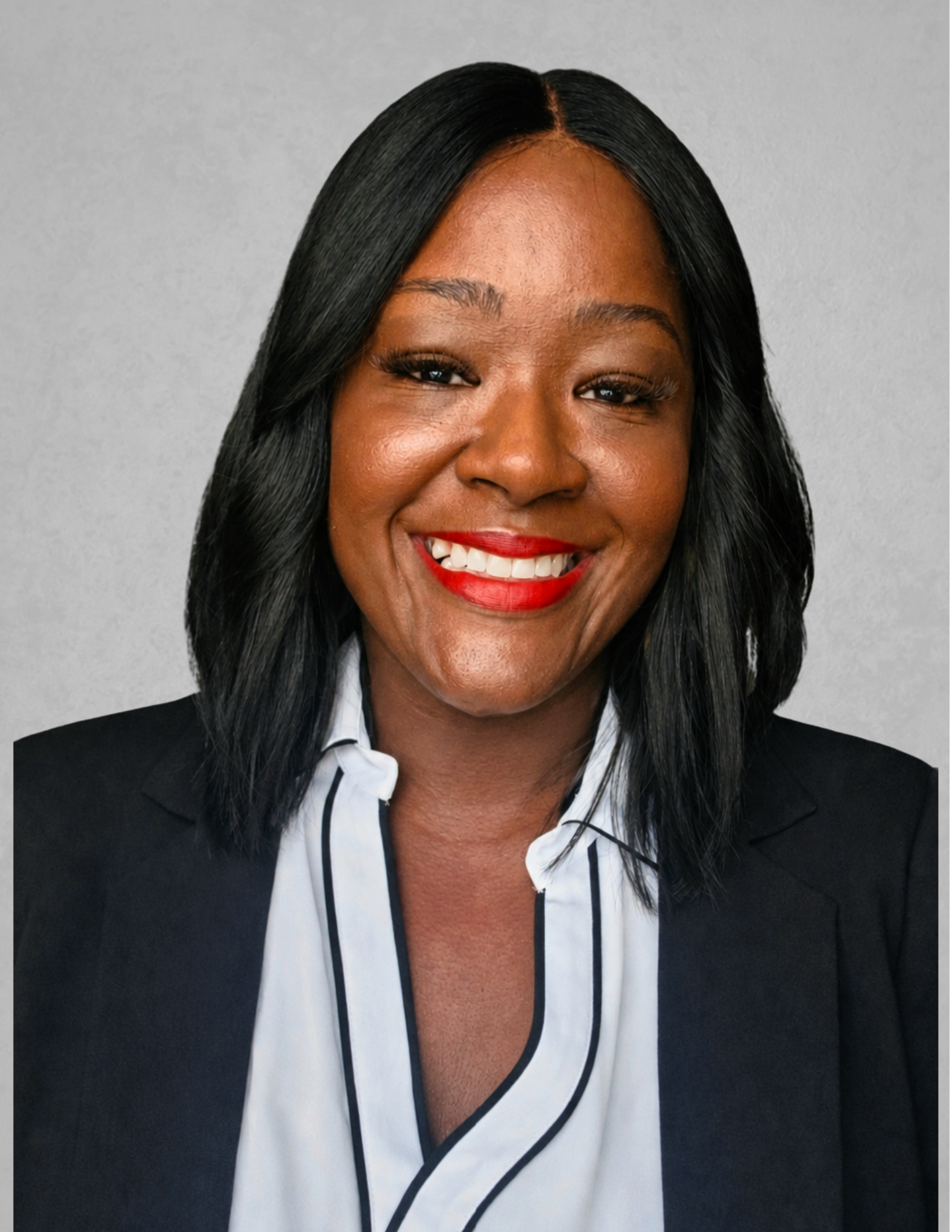 Professional headshot of Elizabeth Campbell-Allen smiling and facing the camera. She is wearing a black blazer over a white blouse with black trim and bright red lipstick. Campbell-Allen has shoulder-length black hair and is posed against a light gray background. The portrait is suitable for use in a school leadership or administrative appointment announcement.