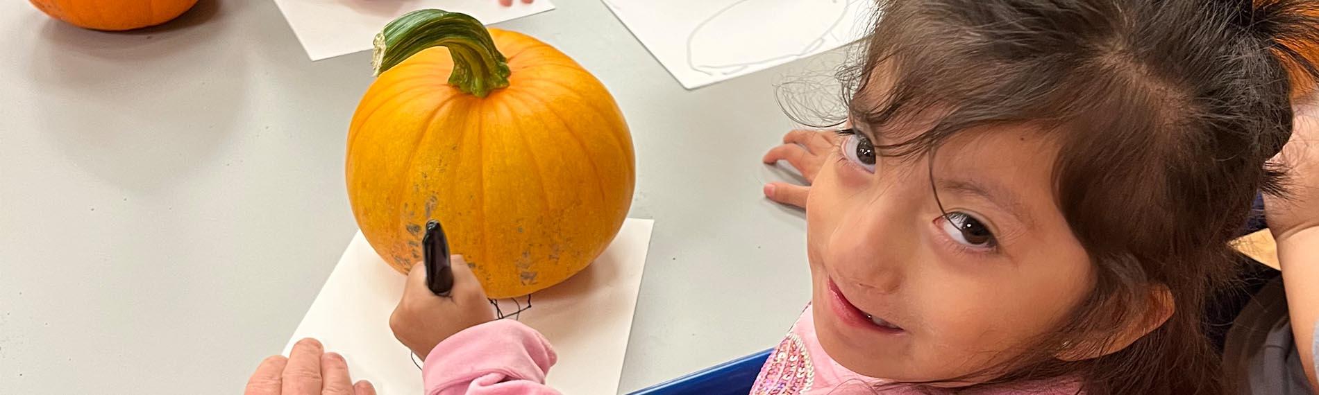 Student smiling up at camera as she traces around a pumpkin