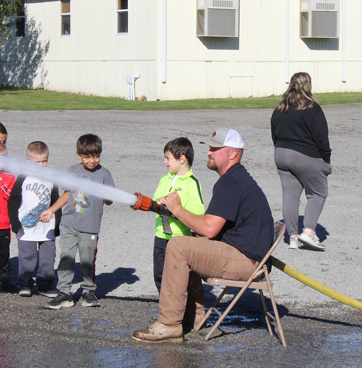 Fire Fighter Andrew Russell helps students with the fire hose