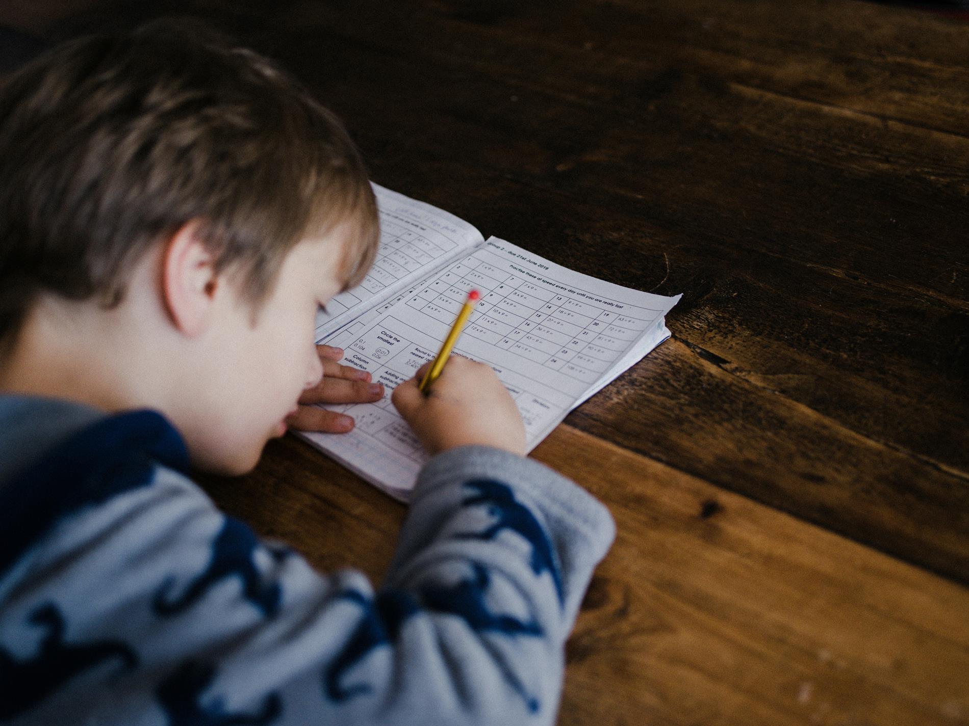 A young boy writes on a piece of paper on a wooden desk