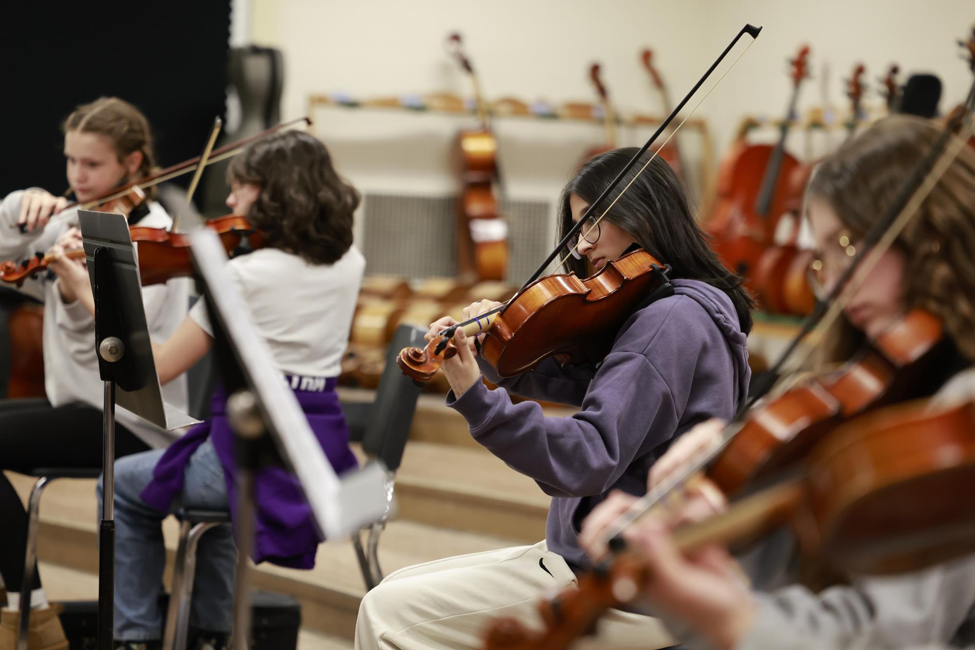 Several middle school students play the violin with sheet music in a band room