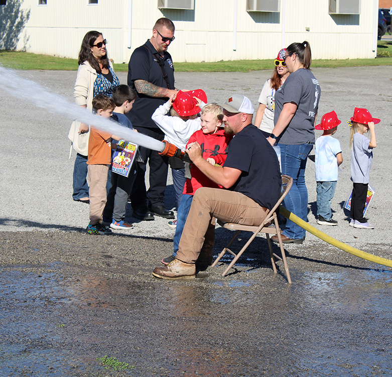 Fire Fighter Andrew Russell helps students with the fire hose