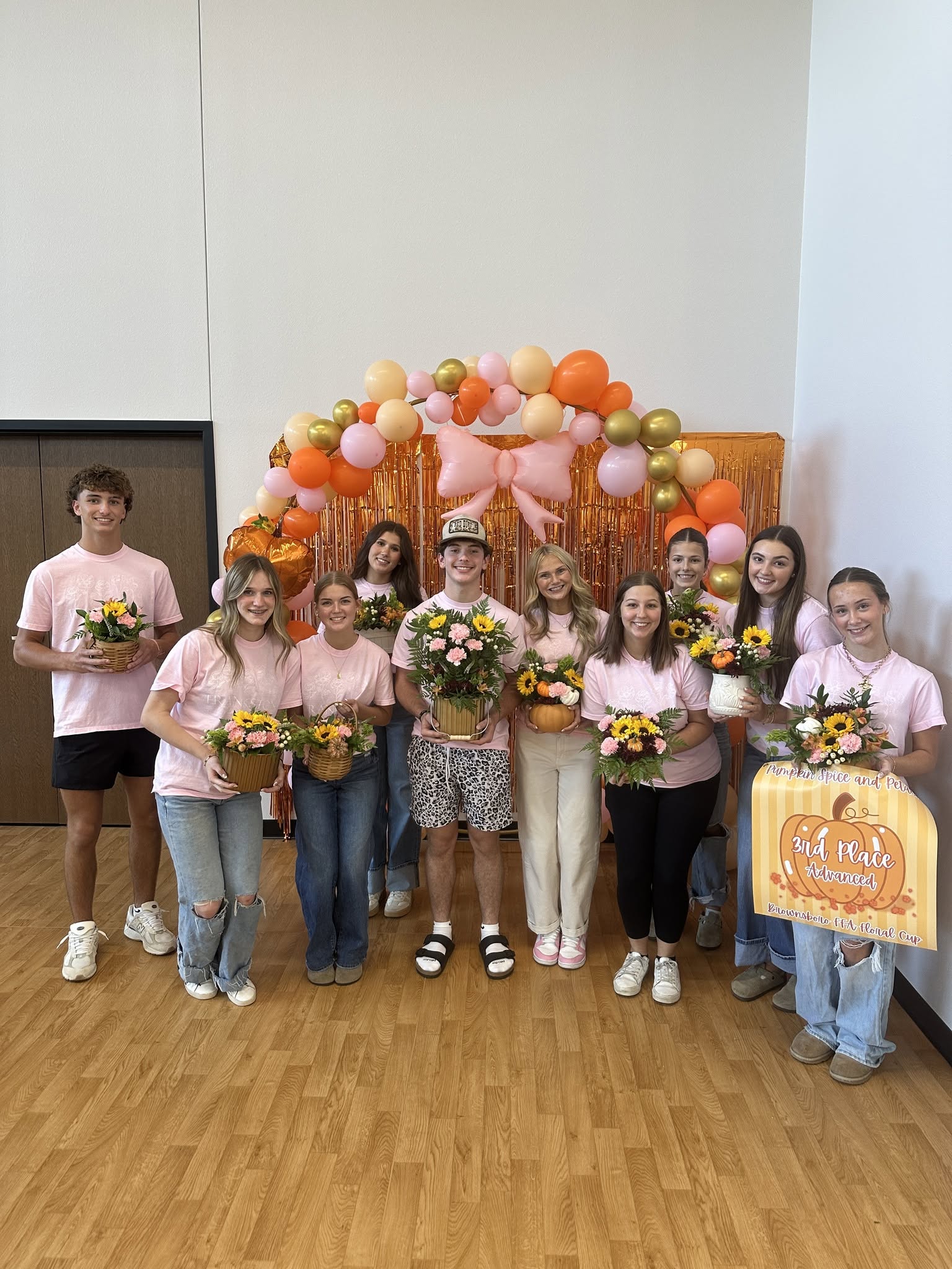 Students holding floral arrangements under a balloon arch at a floral competition.