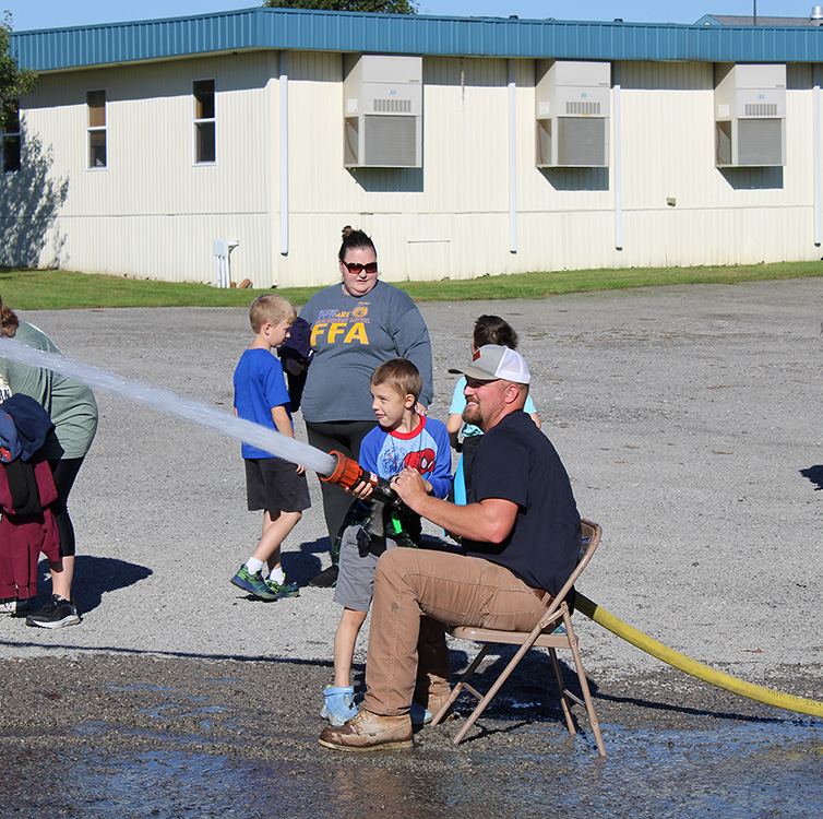 Fire Fighter Andrew Russell helps students with the fire hose