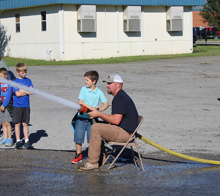 Fire Fighter Andrew Russell helps students with the fire hose