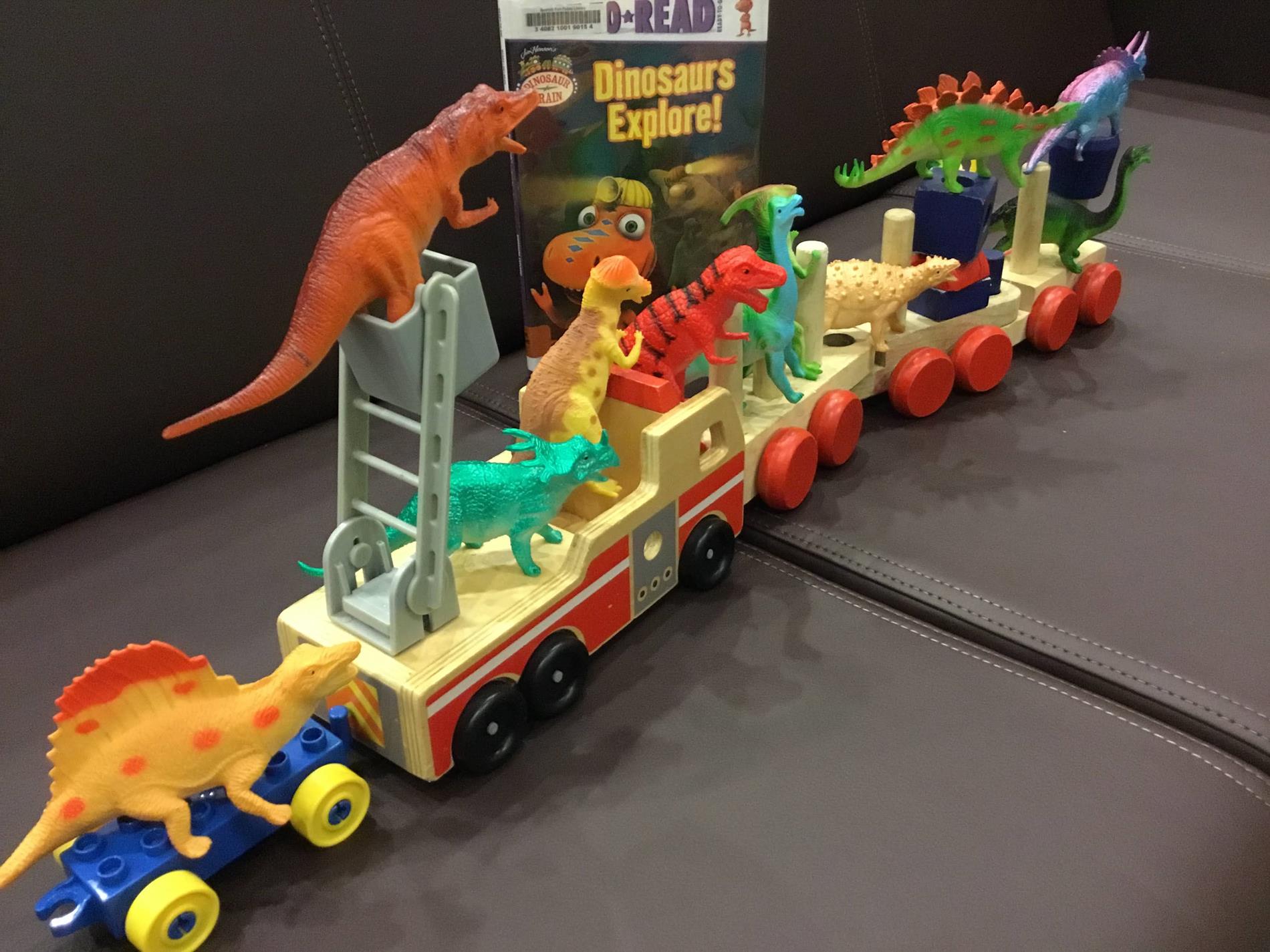 toy dinosaur figures arranged on a toy train made of wooden blocks staged beside a Learn to Read beginning Chapter book version of the title "Dinosaurs Explore" based on the PBS children's television show "Dinosaur Train". Click on photo for link to PBS page