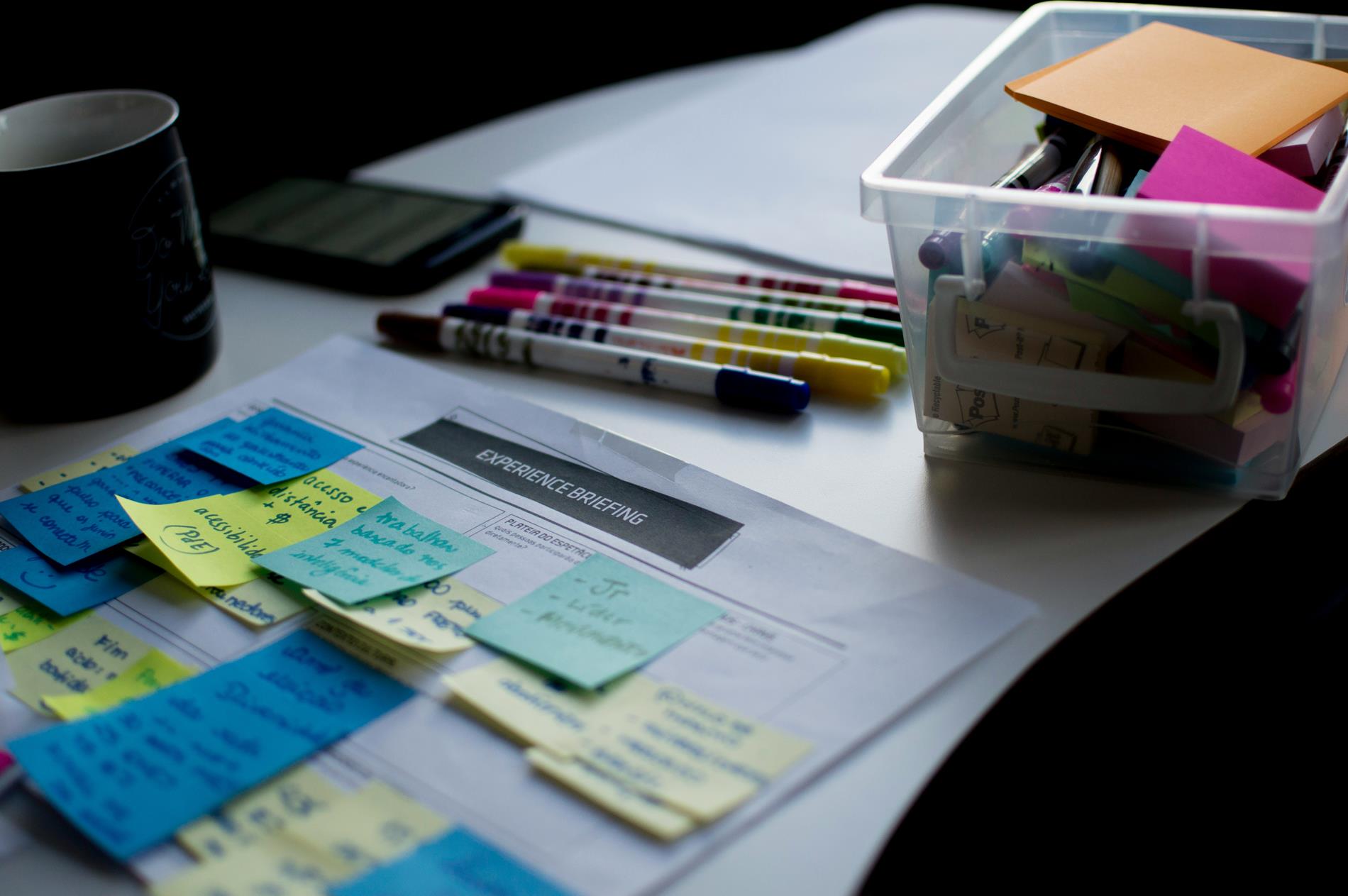 A tote and highlighters sit on a desk with a briefing paper covered in Post-It Notes
