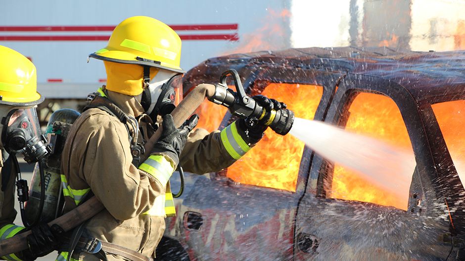 firefighter holding a fire hose wetting a burning car