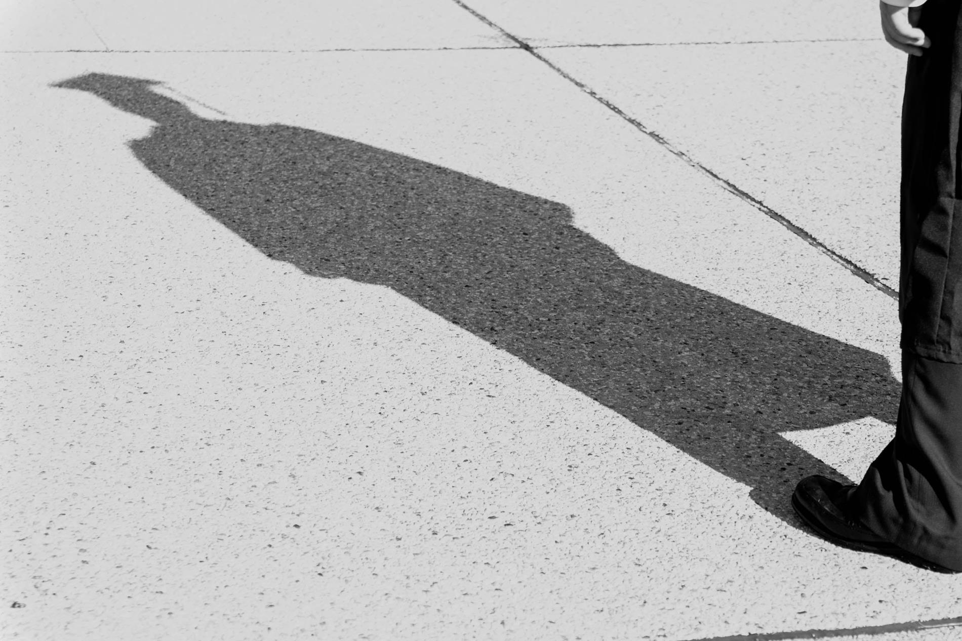 A person with a graduation cap and gown looking at their own shadow on a sidewalk
