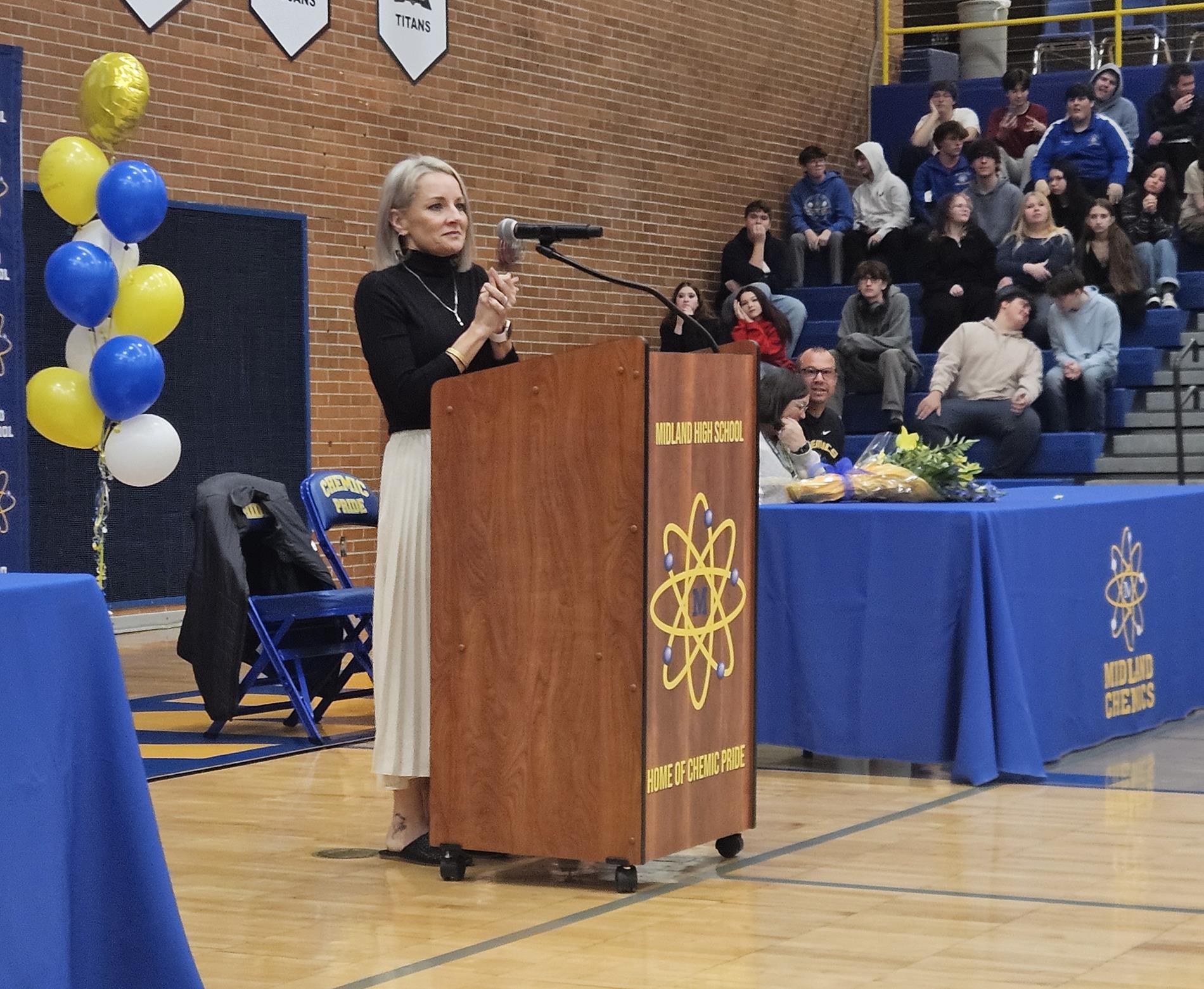 Tiela speaks in the gym at the Midland High podium