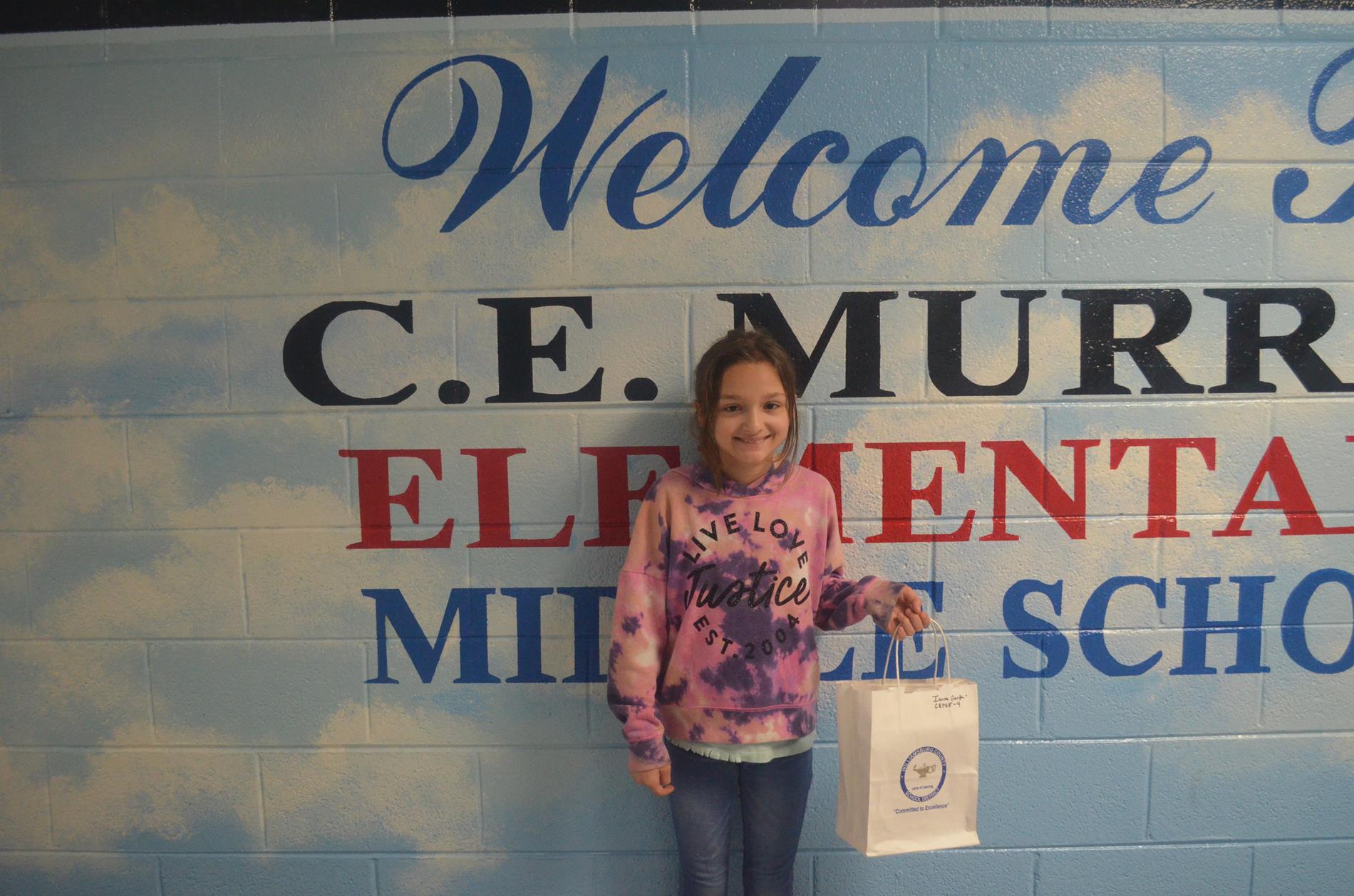 welcome to c.e. murray elementary middle school. student standing in front of wall mural holding gift bag