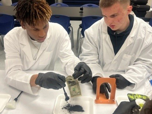 2 male Law & Public Safety students dust bills for fingerprints
