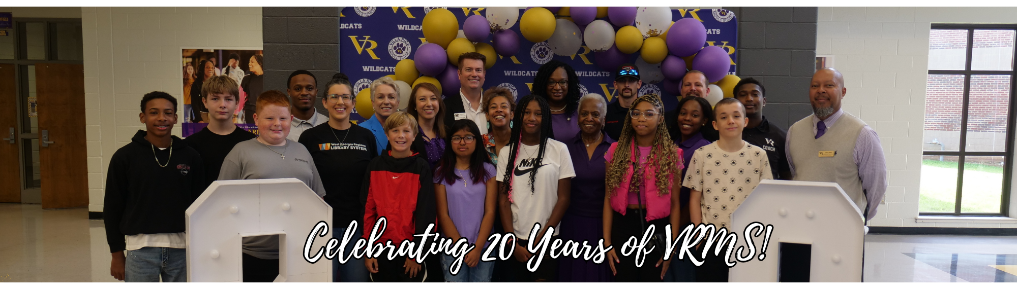 Students, teachers, admin, and community in from of banner for 20 year anniversary