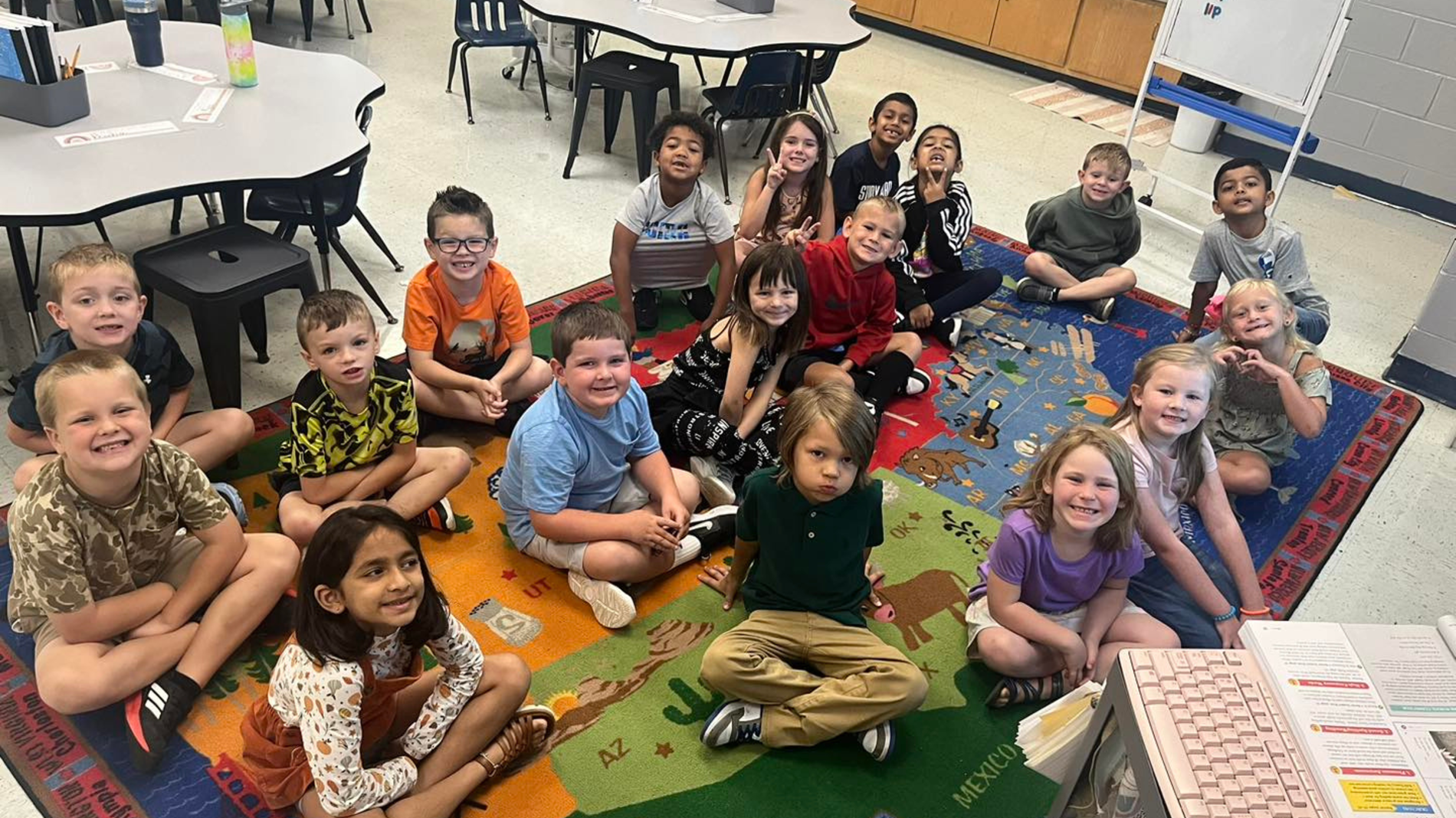 1st grade students are sitting on the classroom rug. They are waiting for their lesson to begin.