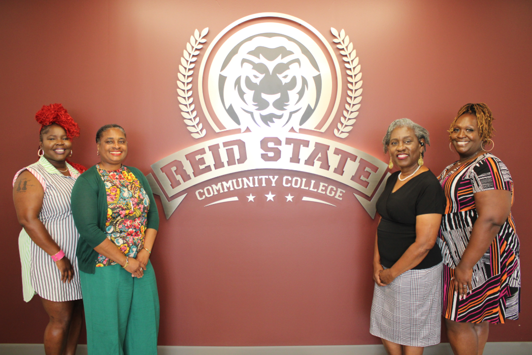 Members of the Reid State Adult Education Department stand in front of the Reid State Logo.