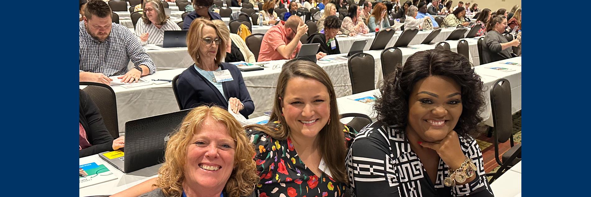 women at G-CASE Conference with crowd ion background