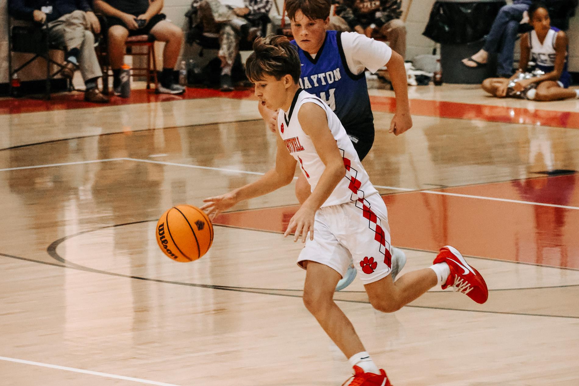 Boys basketball player dribbling ball past midcourt