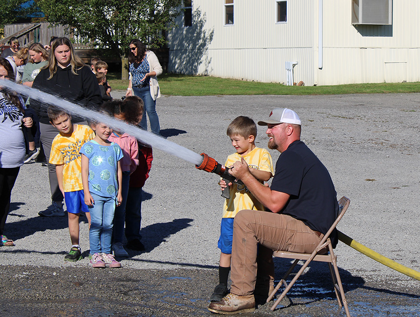 Fire Fighter Andrew Russell helps students with the fire hose