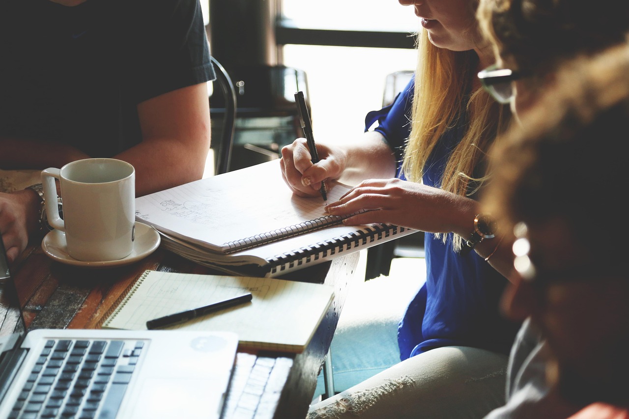 A group of people around a table with a woman taking notes in a notebook