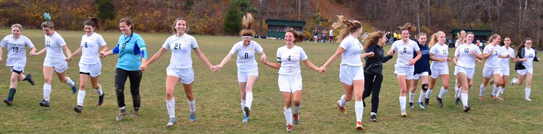 The girls soccer team holds hands and runs across the field
