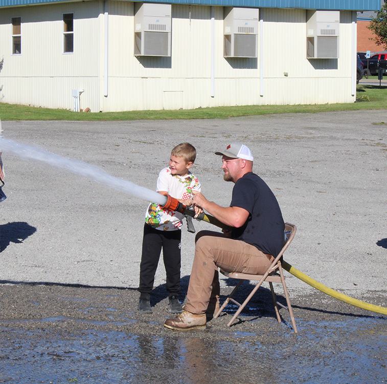 Fire Fighter Andrew Russell helps students with the fire hose