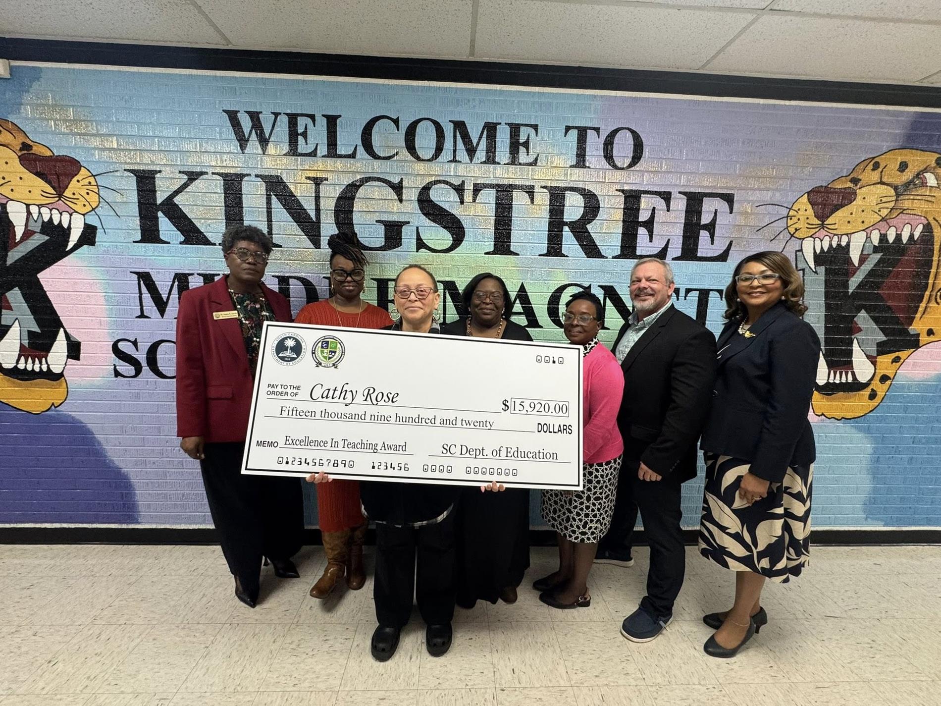people standing in hallway holding large check 