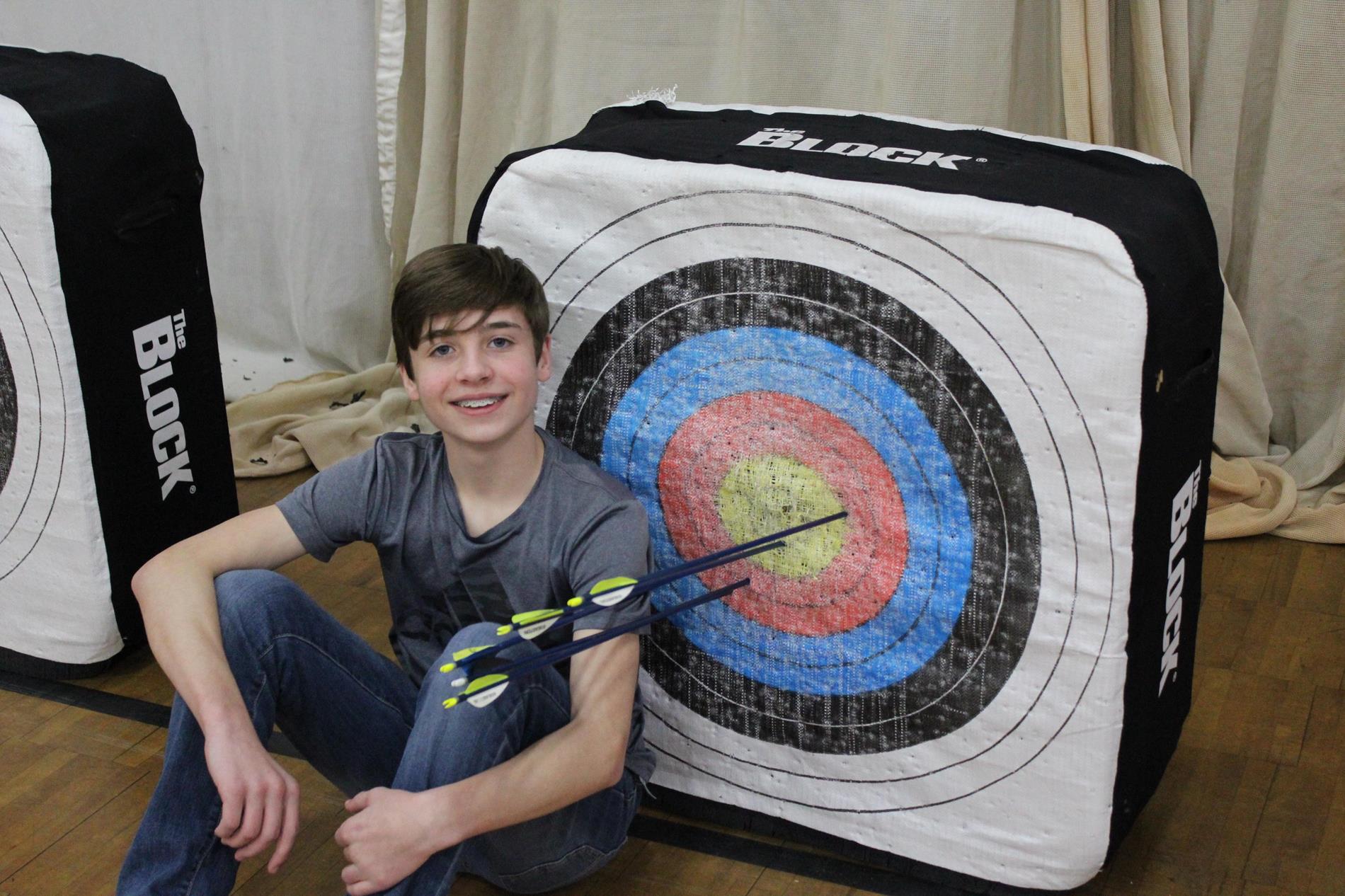 Student sitting next to archery target with arrows sticking out