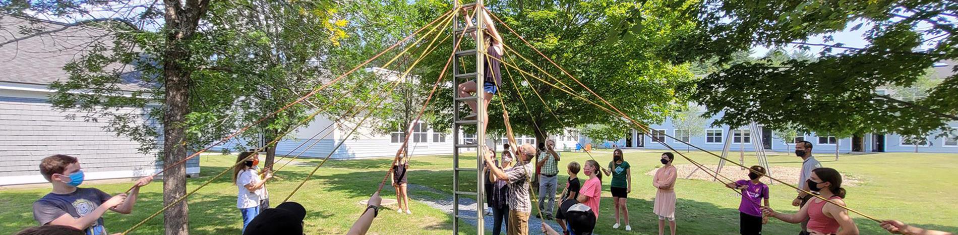 a group of middle schoolers and their teachers in a circle do an activity with a ladder and ropes