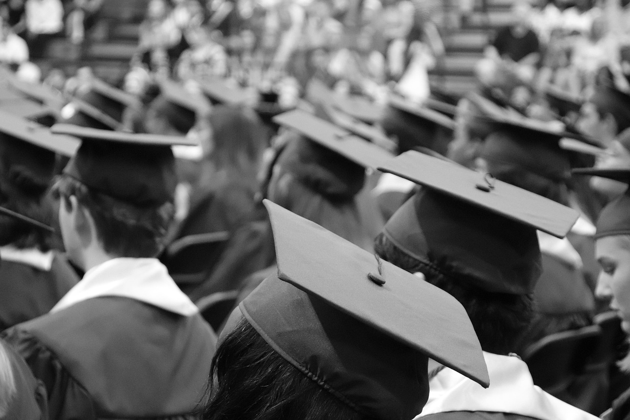 A black and white photo of students in graduation caps and gowns taken from the back