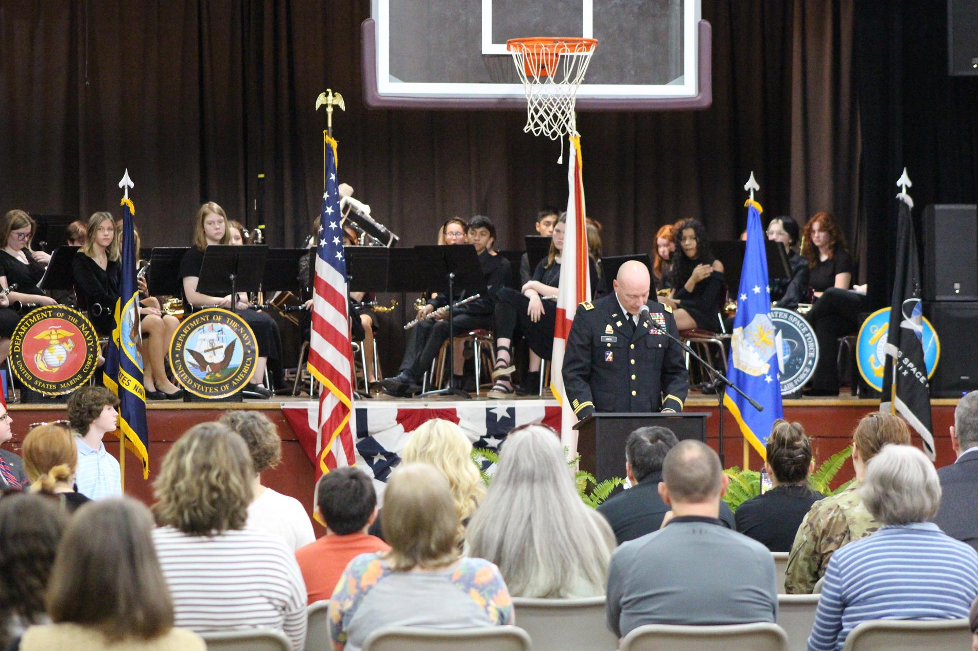 crowd seated in PJHS gym facing a speaker in military uniform