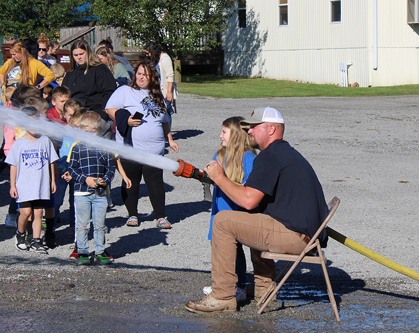 Fire Fighter Andrew Russell helps students with the fire hose